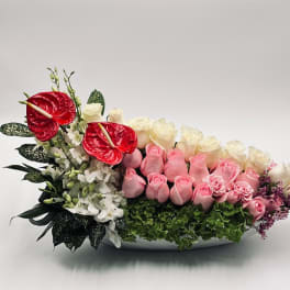Pink and white roses with red anthuriums in a low white bowl