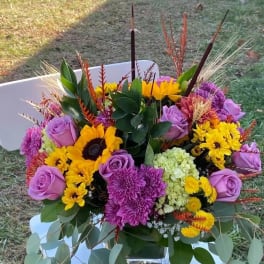 Colorful bouquet with purple roses, yellow sunflowers, and chrysanthemums in a glass vase