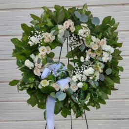 Large white floral wreath on a stand with a lavender ribbon