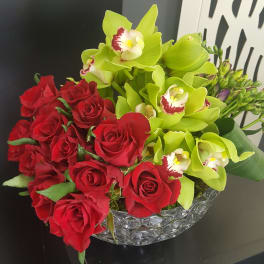 Red roses and lime green orchids arranged in a clear glass bowl