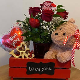 Red roses in a vase with a teddy bear and heart balloons