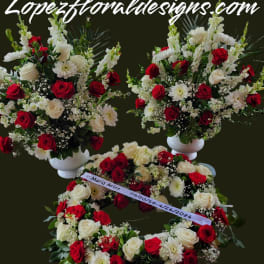 Red and white rose arrangements with white daisies in pedestal vases and a wreath