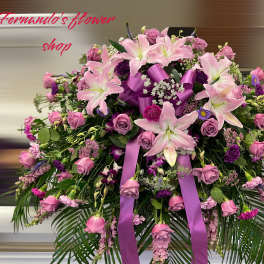 Large pink and purple lily and rose spray with bow and palm fronds on a stand