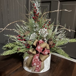 Holiday arrangement with evergreen branches, red berries, and a decorative bow in a round container