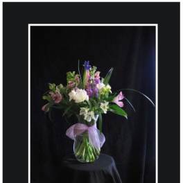 Mixed bouquet of pink, purple, and white flowers in a glass vase with a lavender bow