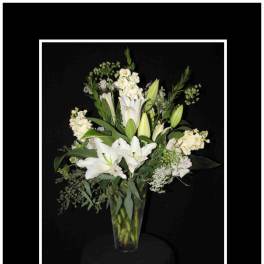 White lilies and mixed white flowers in a tall glass vase