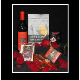 Wine bottle, crackers, chocolate, and a jar arranged with red rose petals