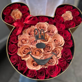 Heart-shaped box filled with red and peach roses, with a ribbon bow and bunny face decoration