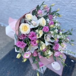 Bouquet of cream roses, pink lisianthus, and white orchids wrapped in pink paper