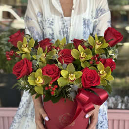 Red roses and yellow orchids arranged in a round red box with a ribbon
