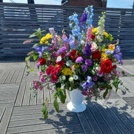 Large mixed bouquet in a white pedestal vase with red, purple, blue, and yellow flowers