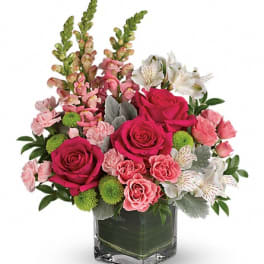 Pink roses and mixed blooms arranged in a square glass vase