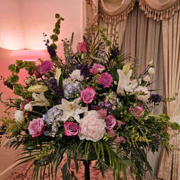 Large mixed floral arrangement on a stand with pink, white, and purple blooms