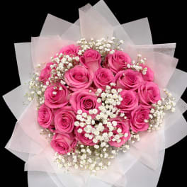 Bouquet of bright pink roses with white baby's breath in pale wrapping