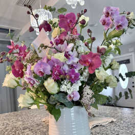 Tall arrangement of pink and purple orchids with white roses in a white ceramic vase