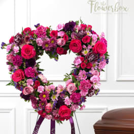 Heart-shaped floral wreath with pink, red, and purple blooms on a stand