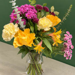 Mixed bouquet of yellow, pink, and purple flowers in a clear glass vase