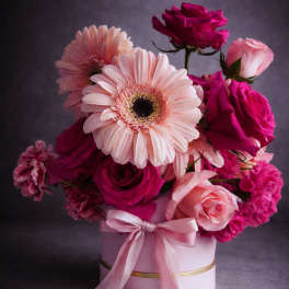 Pink and magenta flower arrangement in a round box with a ribbon
