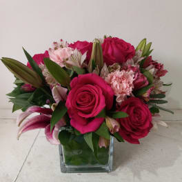 Pink roses and lilies arranged in a square glass vase