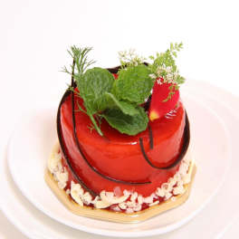 Small red glazed cake topped with fresh herb sprigs on a white plate