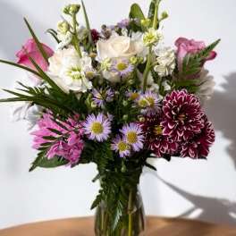 Mixed bouquet of white, pink, and purple flowers in a clear glass vase