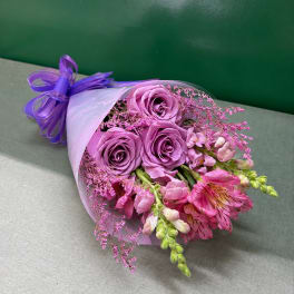 Bouquet of lavender roses and pink flowers wrapped in white paper with a purple ribbon