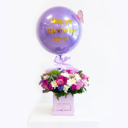 Birthday balloon above a mixed flower arrangement in a pink box