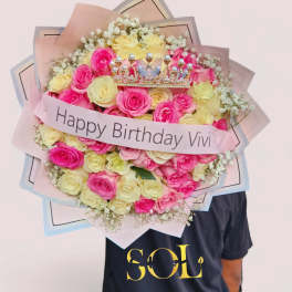 Bouquet of pink and pale yellow roses with a birthday ribbon and crown