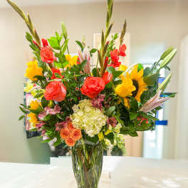 Bright mixed bouquet in a glass vase with sunflowers, roses, and lilies