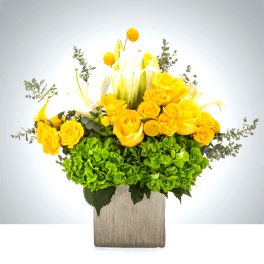 Yellow roses and white calla lilies in a square wooden vase