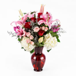 Pink lilies, red roses, and white hydrangeas in a red glass vase
