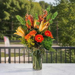 Tall orange and yellow floral arrangement in a clear glass vase