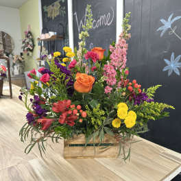Mixed bouquet in a wooden crate with orange roses and pink, yellow, and purple flowers