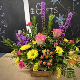 Mixed bouquet with pink roses, yellow daisies, and purple flowers in a wooden box