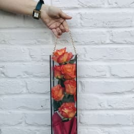 Tall box of orange roses with a pink wrap and chain handle