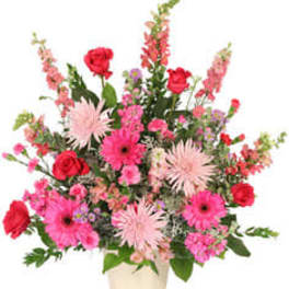 Pink and red mixed flower arrangement in a cream vase