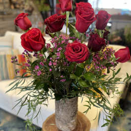 Red roses arranged in a rustic vase with small pink filler flowers