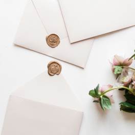 Three cream envelopes with wax seals beside pink flowers