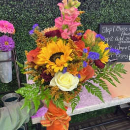 Bright mixed bouquet with sunflowers, roses, and snapdragons in an orange wrap