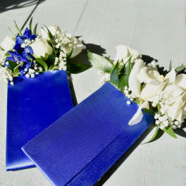 Two blue ribbon corsages with white flowers on a light surface