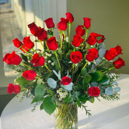 Red roses arranged in a clear glass vase with small white filler flowers