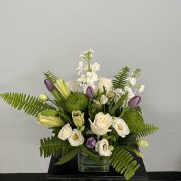 White and purple floral arrangement in a glass vase with green accents
