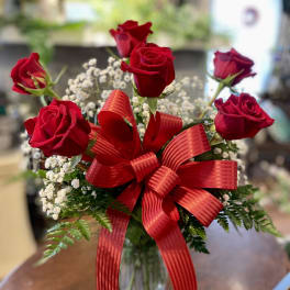 Red roses in a glass vase with a large red ribbon and baby's breath
