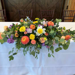 Long floral centerpiece with mixed blooms and trailing greenery on a table