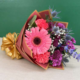 Pink and purple mixed bouquet wrapped in burgundy paper with a gold ribbon