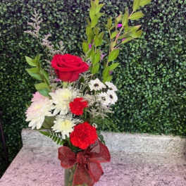 Red roses and white daisies in a glass vase with a red bow