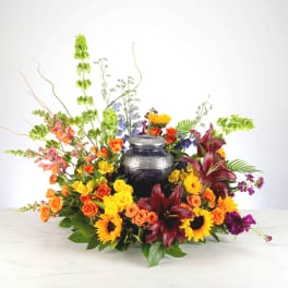 Colorful floral arrangement around a dark urn with orange, yellow, and burgundy blooms