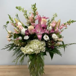 Pink lilies and white blooms arranged in a clear glass vase