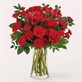 Arrangement of red roses, carnations, and alstroemeria in a clear glass vase
