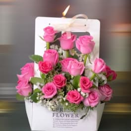 Pink roses arranged in a white gift bag with a ribbon handle